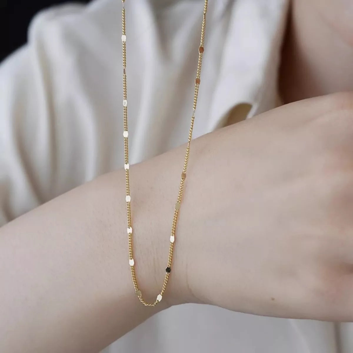 Gold beaded necklace on a person's wrist with a neutral background