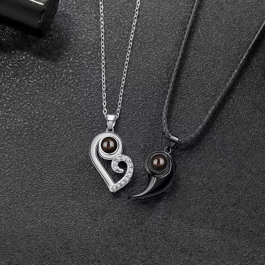 Two pendants, one silver and one black, on a dark textured surface.