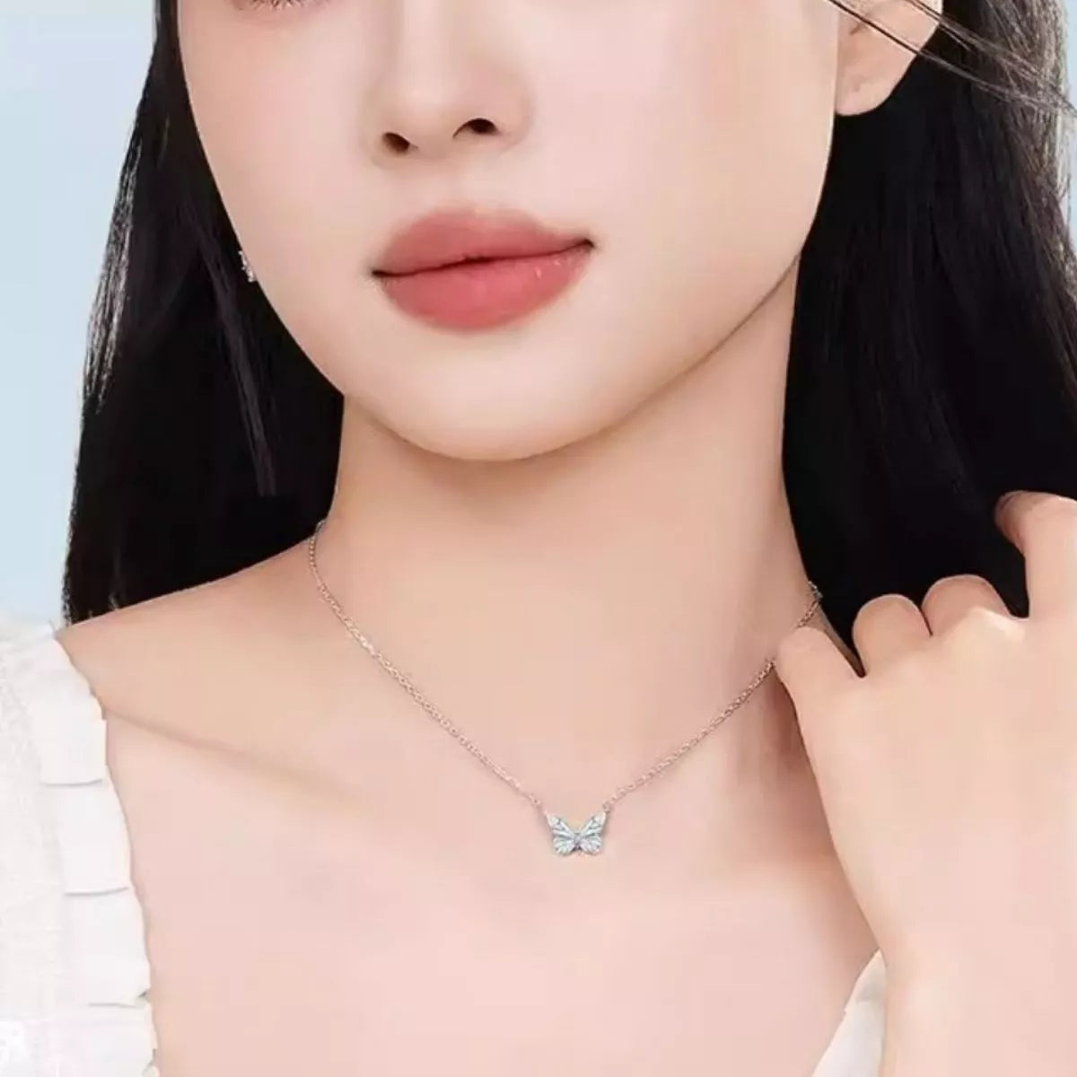 Close-up of a person wearing a delicate butterfly necklace against a light background