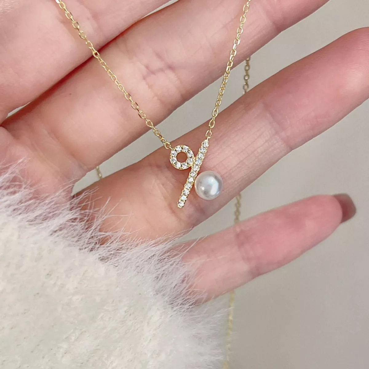 Gold necklace with a pearl pendant held by a hand on a neutral background