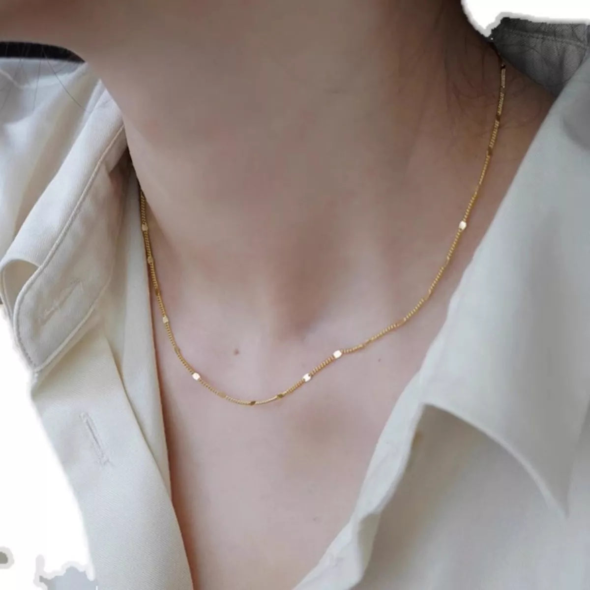 A gold necklace worn by a person with a light background
