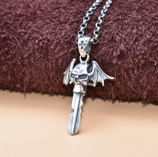 Silver pendant with a skull and wings on a chain against a brown fabric background