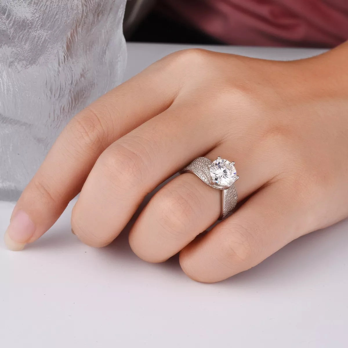 Silver ring with a diamond on a finger against a neutral background