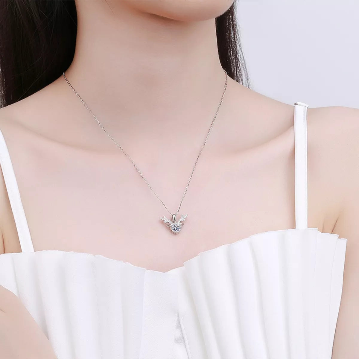 Woman wearing a delicate silver necklace with a small pendant against a plain background