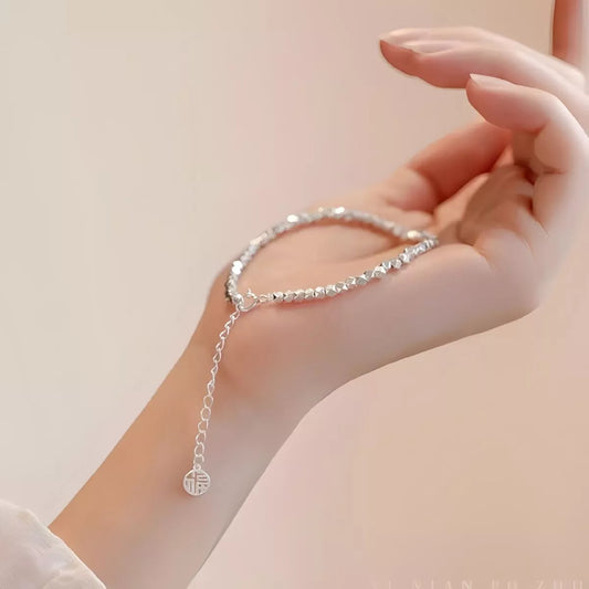 Silver bracelet with a small charm on a hand against a light background