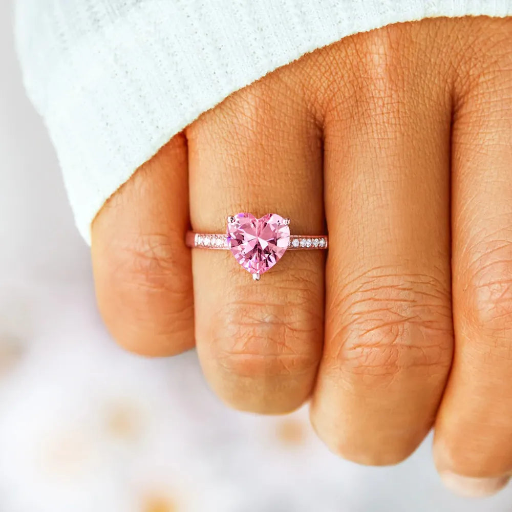 Heart-shaped pink gemstone ring on a finger with a blurred background