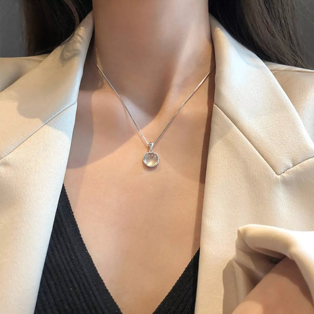 Necklace with a pendant worn by a person in a light-colored blazer.