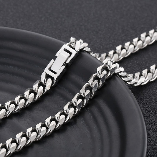 A close-up of a silver-toned metal chain necklace with a rectangular clasp, draped across a dark round plate on a dark textured background.