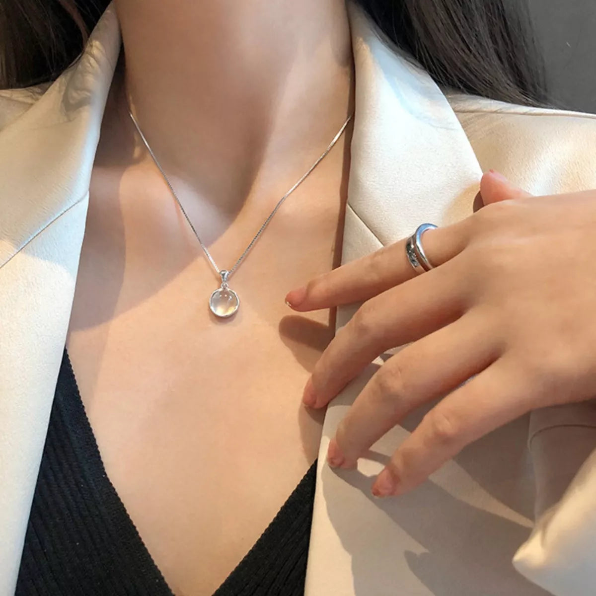 Person wearing a silver necklace with a pendant, holding their hand near the neck.