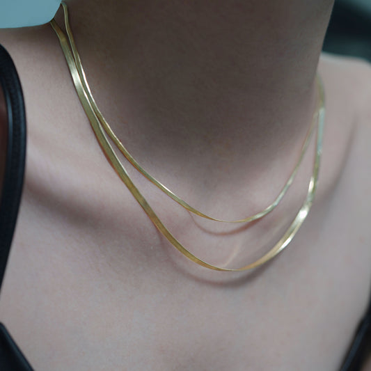Gold necklace on a person's neck with a neutral background
