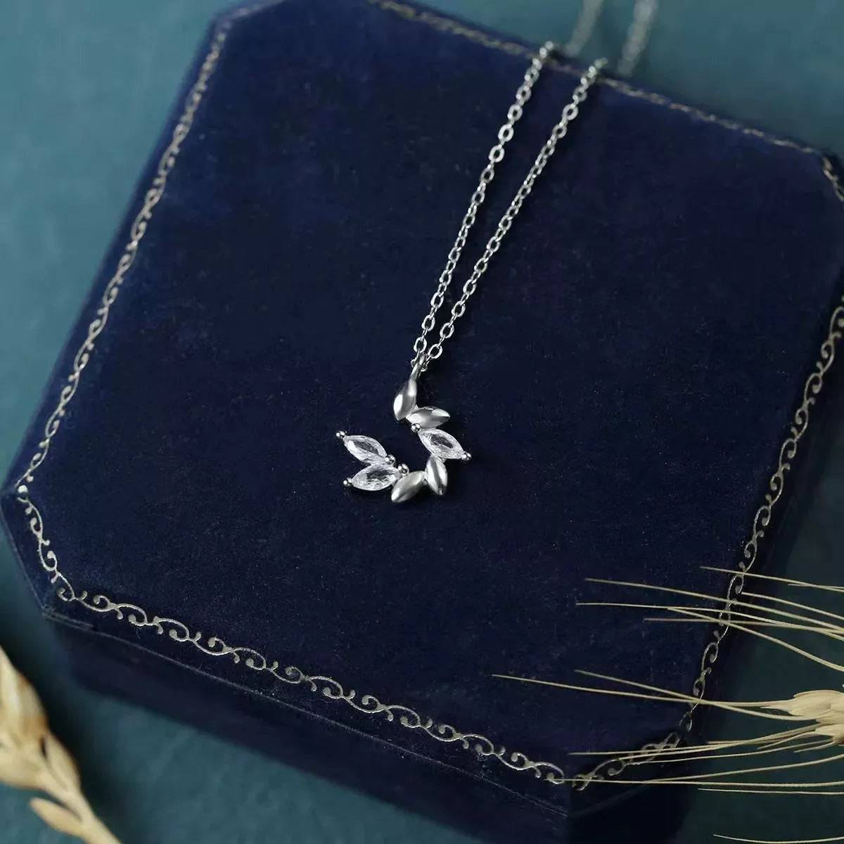 Silver necklace with leaf pendant on a blue velvet surface