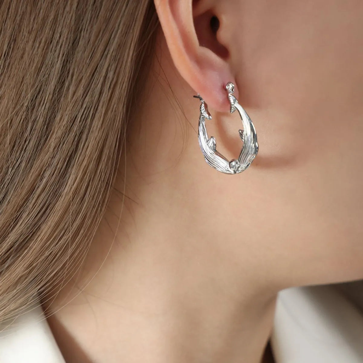 Silver hoop earring worn by a person with light brown hair.