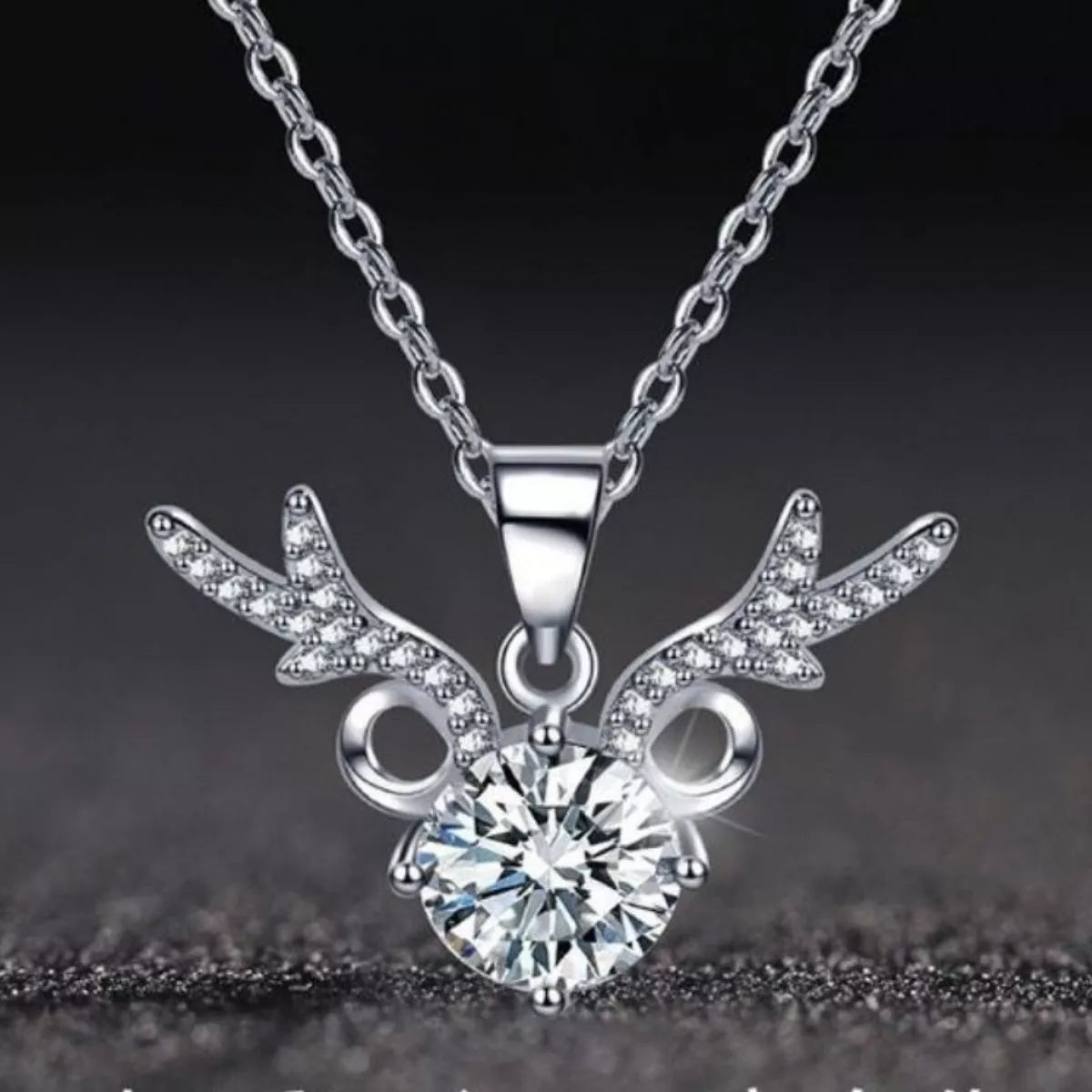Silver deer head necklace with a clear gemstone on a dark background