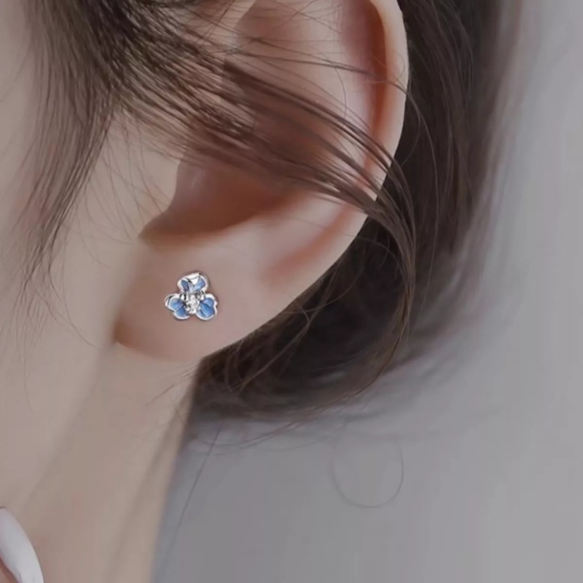 Close-up of an ear wearing a floral earring with blue stones on a neutral background