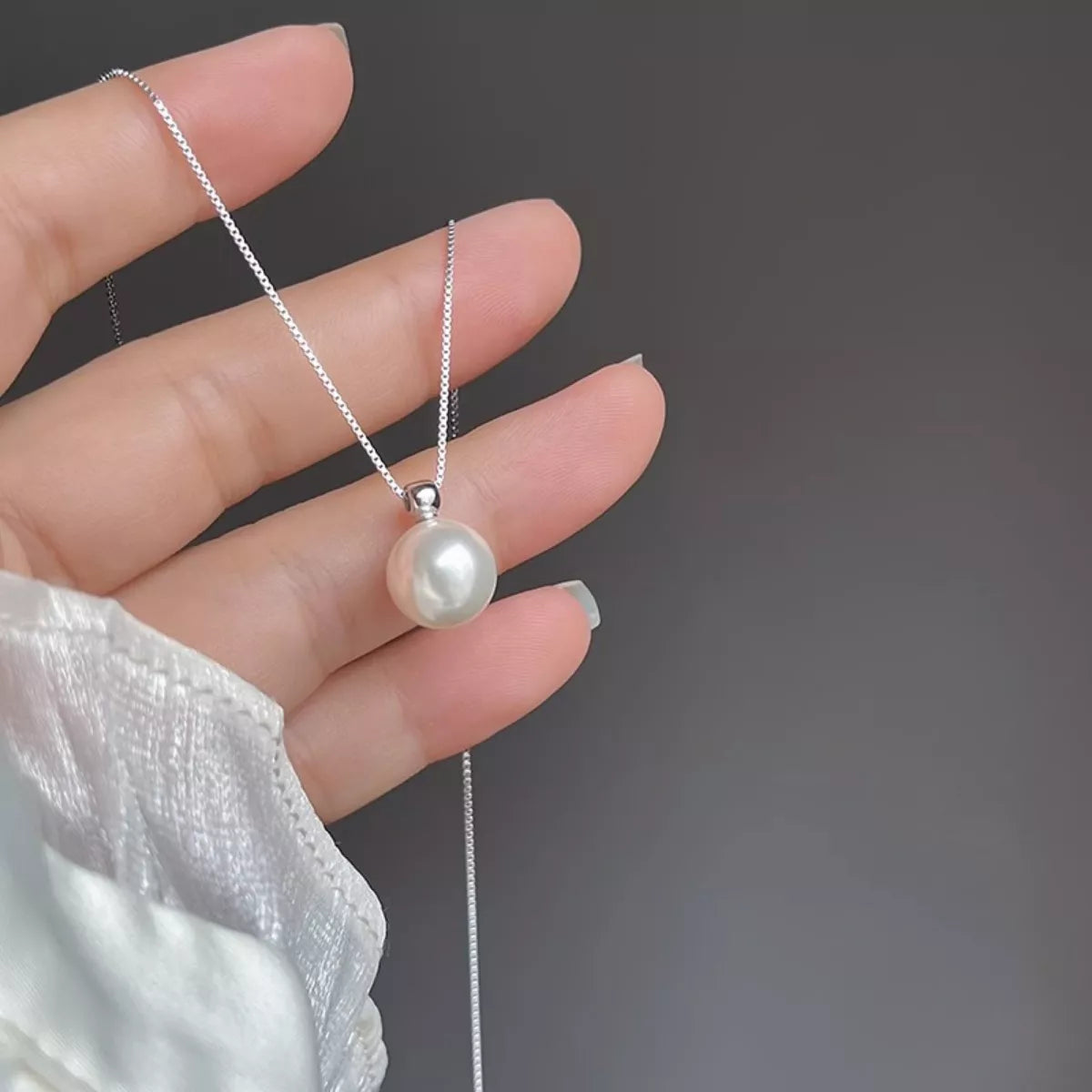 Pearl necklace held by a hand against a dark background