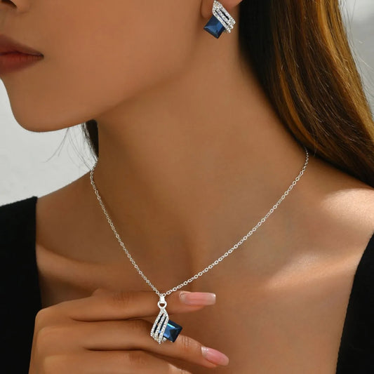 Woman wearing a silver necklace with a blue pendant and matching earrings.