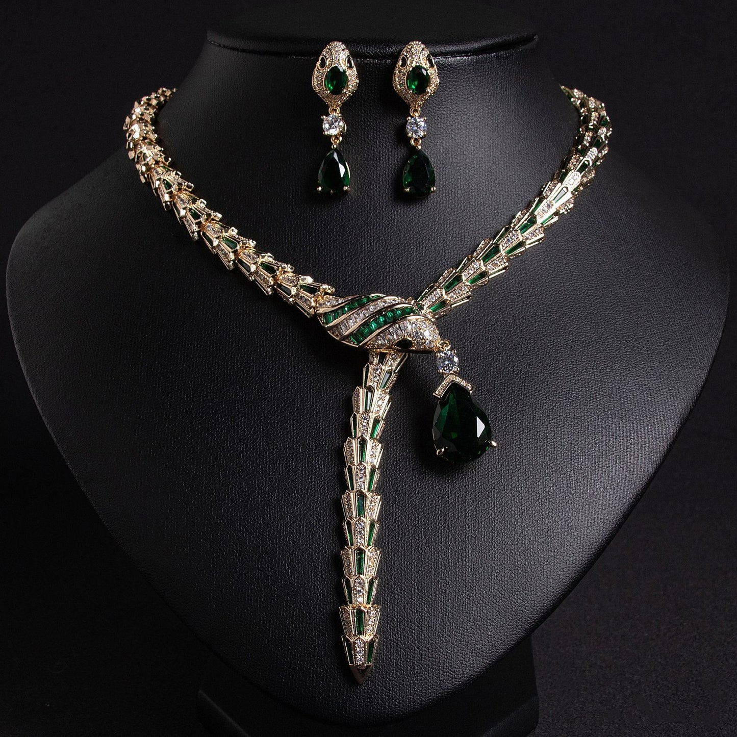 Gold snake necklace and earrings set with emerald green and clear stones, on a black bust.