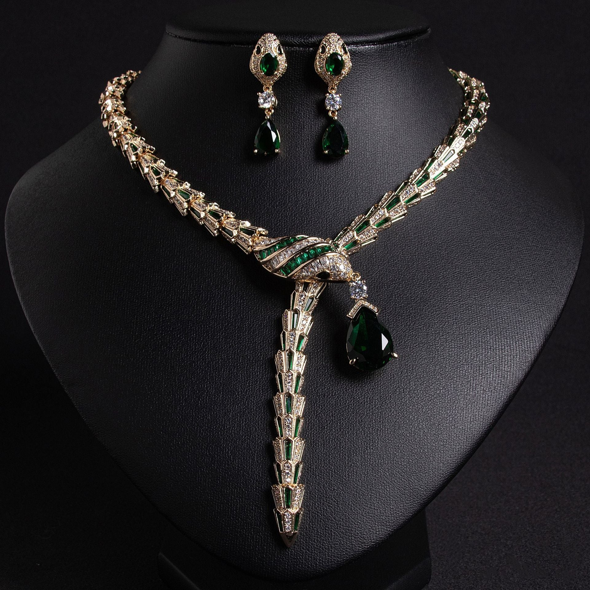 Gold snake necklace and earrings set with emerald green and clear stones, on a black bust.