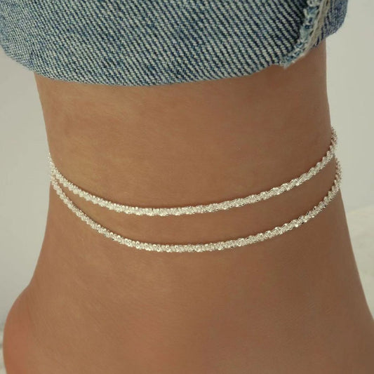 Silver anklets on a person's ankle with a denim background
