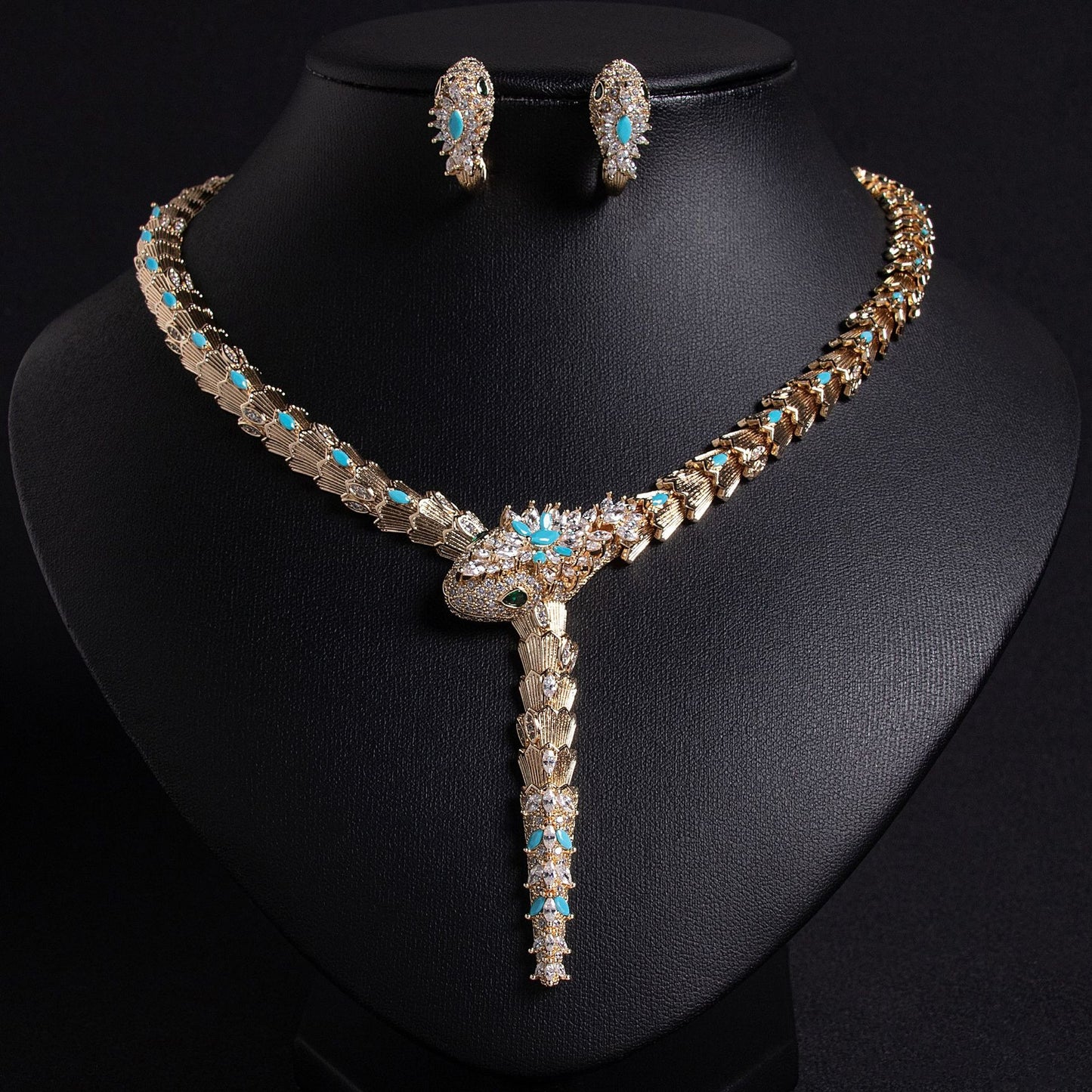 Gold snake necklace and earrings set with turquoise blue and clear stones on a black background.