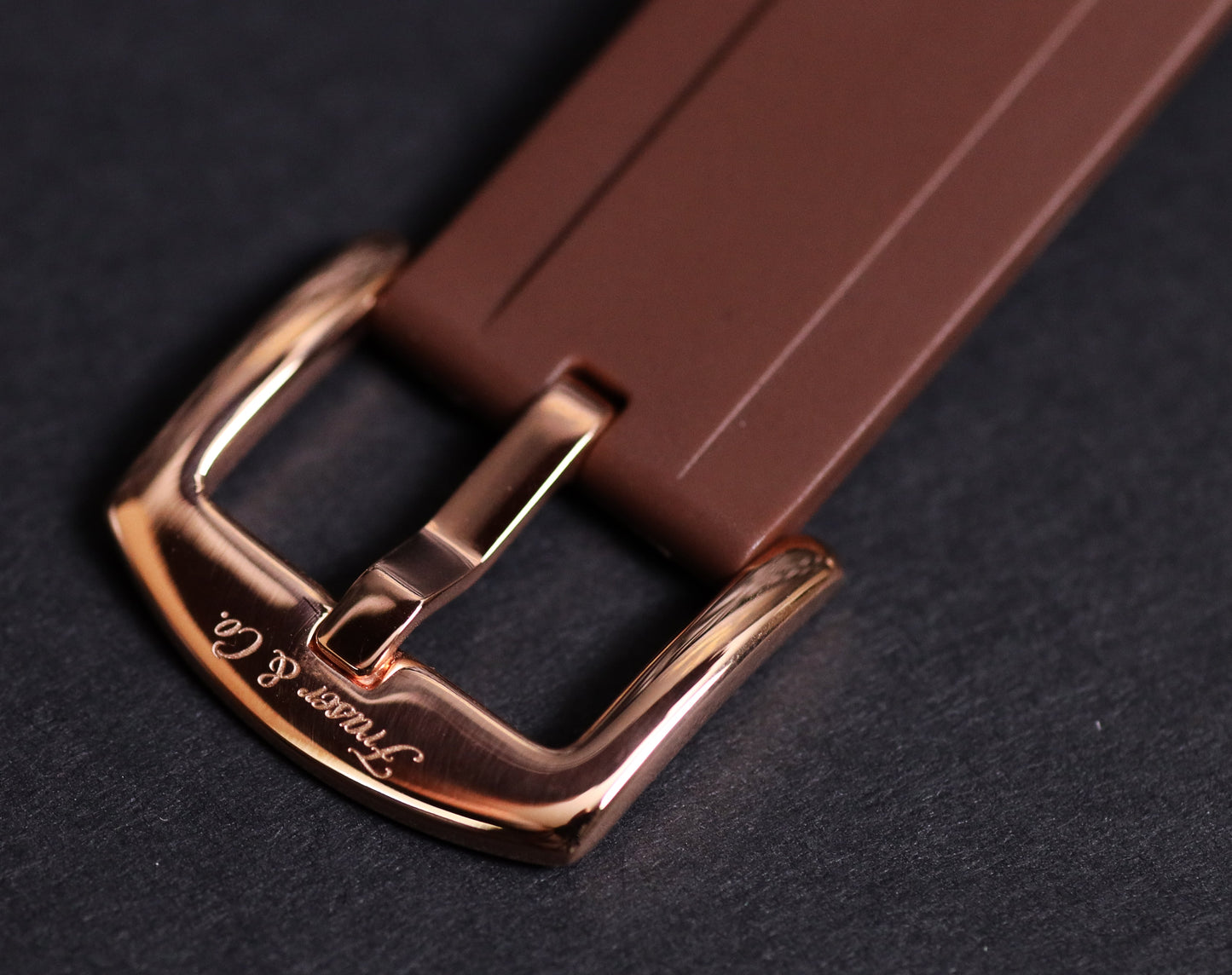 Brown watch strap with rose gold buckle on a dark background