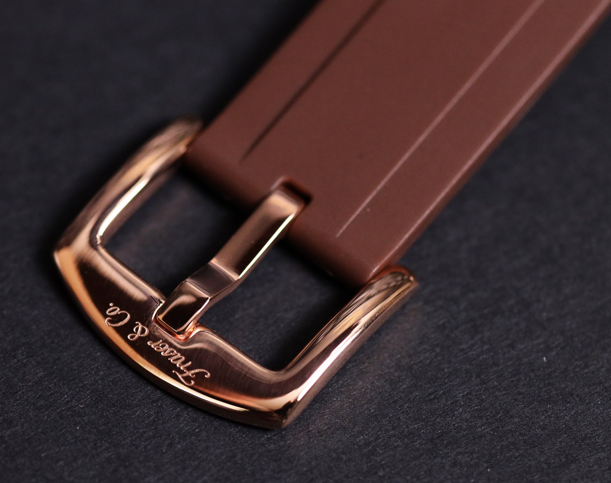 Brown watch strap with rose gold buckle on a dark background