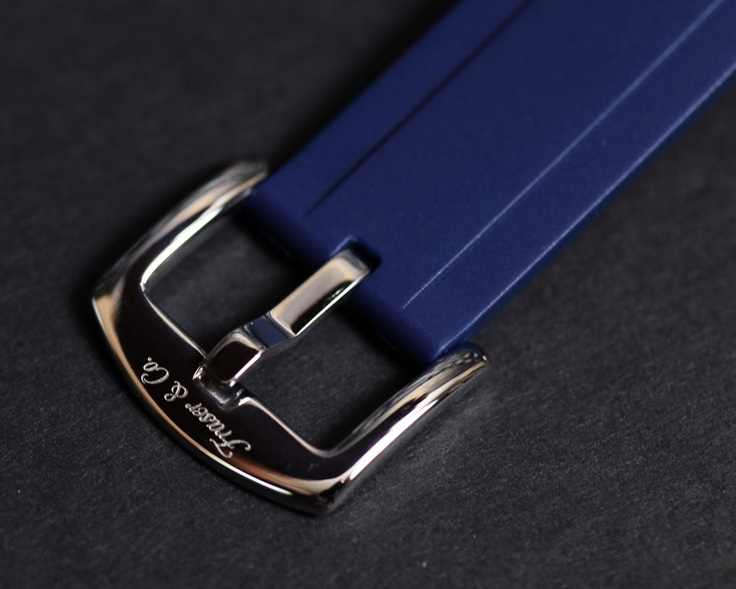 Close-up of a blue watch strap with a silver buckle on a dark background